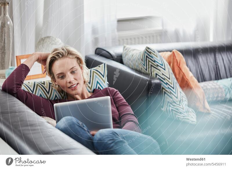 Junge Frau mit Tablette liegt auf der Couch zu Hause Zuhause daheim Tablet Computer Tablet-PC Tablet PC iPad Tablet-Computer Sofa Couches Liege Sofas weiblich