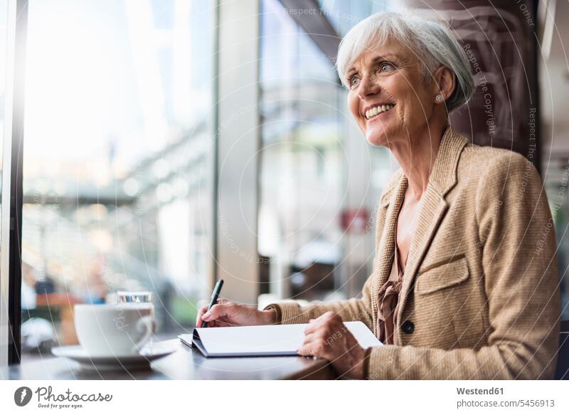 Lächelnde ältere Geschäftsfrau, die in einem Café Notizen macht Geschäftsfrauen Businesswomen Businessfrauen Businesswoman notieren Cafe Kaffeehaus Bistro Cafes