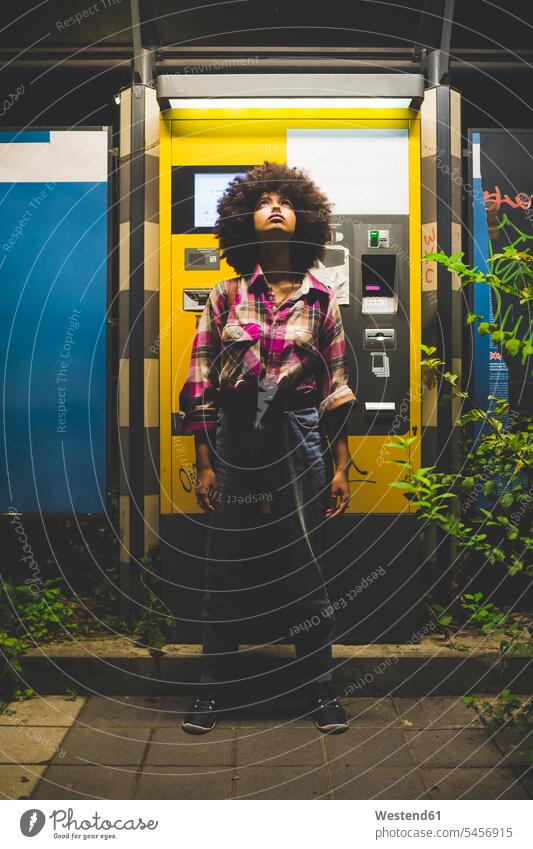 Junge Frau mit Afrofrisur steht nachts am Fahrkartenautomaten und schaut auf Leute Menschen People Person Personen gelockt gelockte Haare gelocktes Haar lockig