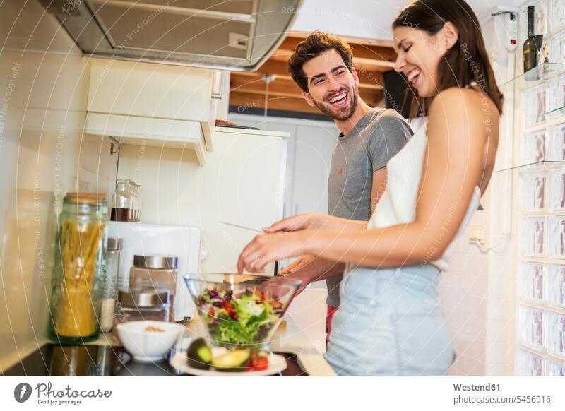 Fröhliches junges Paar bereitet zu Hause in der Küche gemeinsam das Essen Farbaufnahme Farbe Farbfoto Farbphoto Spanien Freundschaft Kameradschaft Freunde
