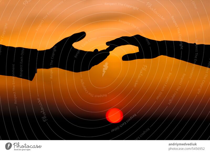 Valentinstag. Silhouette der Hände der Frau und des Mannes, die sich gegenseitig erreichen, berühren Finger mit Zärtlichkeit auf orange Sonnenuntergang Himmel Hintergrund. Helfende Hände, speichern und unterstützen Menschen Konzept. Freundschaft.