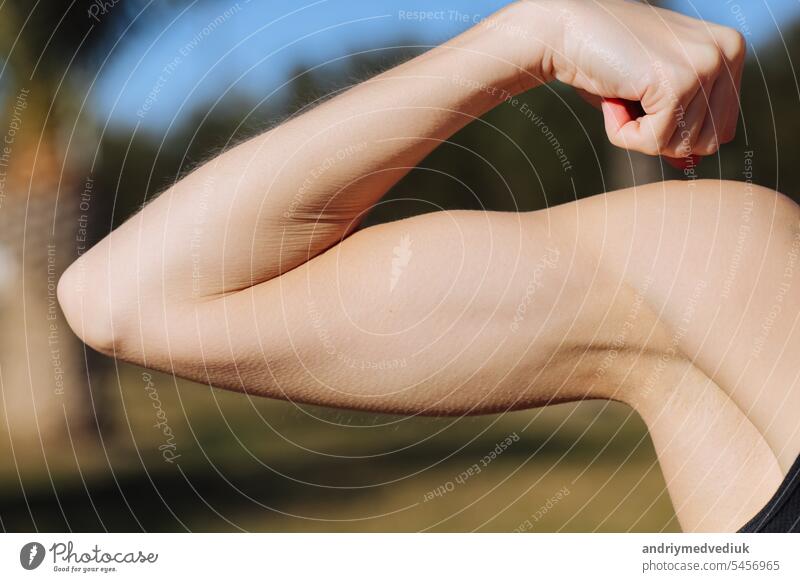 Abgeschnittenes Foto des Arms einer jungen Frau mit Muskeln, Bizeps auf Naturhintergrund. Mädchen Nahaufnahme von demonstriert starke Hand nach dem Training, Fitness, sportliche Aktivitäten im Freien. Weltgesundheitstag