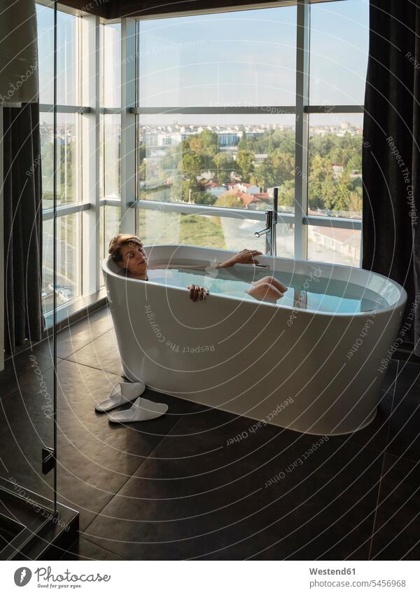 Frau badet in Badewanne gegen Fenster in Luxus-Hotelzimmer Farbaufnahme Farbe Farbfoto Farbphoto Innenaufnahme Innenaufnahmen innen drinnen Tag