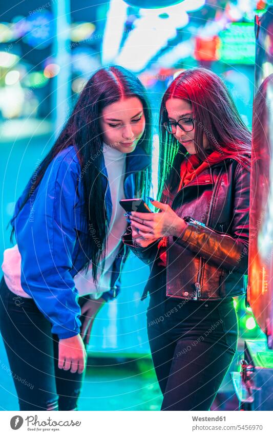 Zwei Teenager-Mädchen teilen sich nachts auf einem Jahrmarkt ein Smartphone Freunde Kameradschaft Freundin Informationen Telekommunikation telefonieren Handies