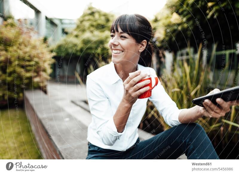 Lächelnde berufstätige Frau hält Kaffeetasse und Smartphone in der Hand, während sie wegschaut Farbaufnahme Farbe Farbfoto Farbphoto Deutschland Geschäftsfrau