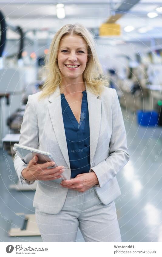 Lächelnde reife blonde Geschäftsfrau mit digitalem Tablet in der Hand, während sie in der beleuchteten Industrie steht Farbaufnahme Farbe Farbfoto Farbphoto