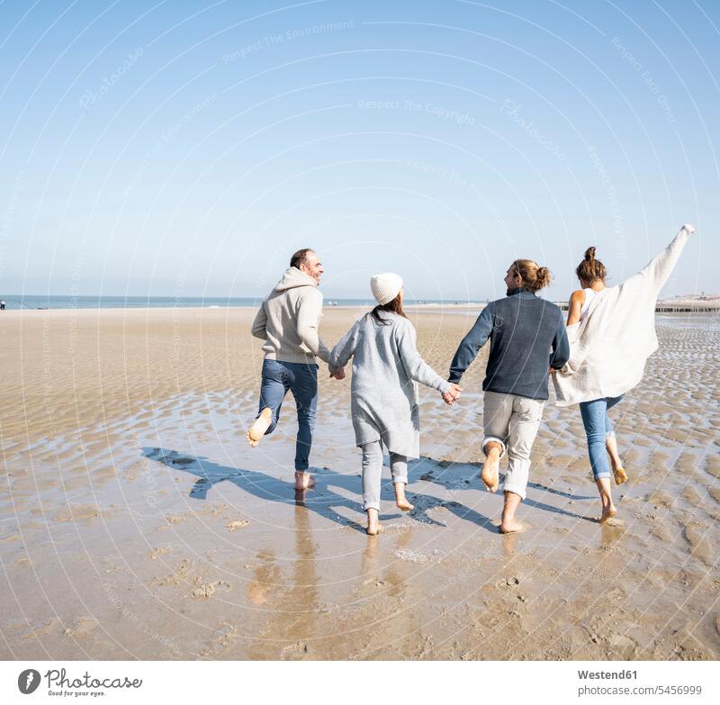 Verspielte Familie hält beim Laufen am Strand Händchen Farbaufnahme Farbe Farbfoto Farbphoto Außenaufnahme außen draußen im Freien Tag Tageslichtaufnahme