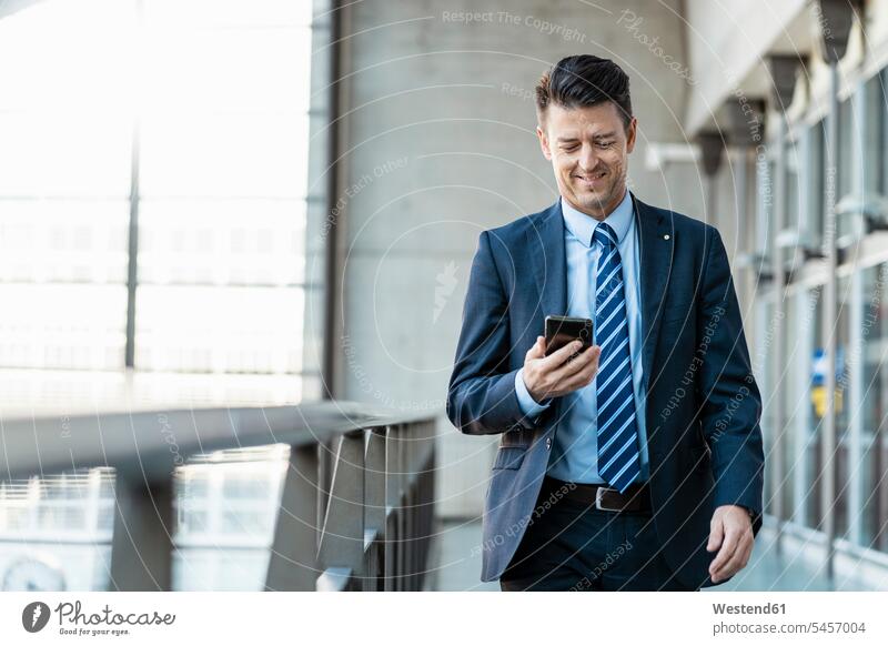 Lächelnder Geschäftsmann mit Mobiltelefon in Bewegung gehen gehend geht Businessmann Businessmänner Geschäftsmänner unterwegs auf Achse Handy Handies Handys