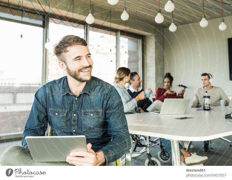 Lächelnder junger Geschäftsmann mit Tablette während einer Besprechung im Büro Arbeitskollege Arbeitskollegen Kollege Job Berufe Berufstätigkeit Beschäftigung