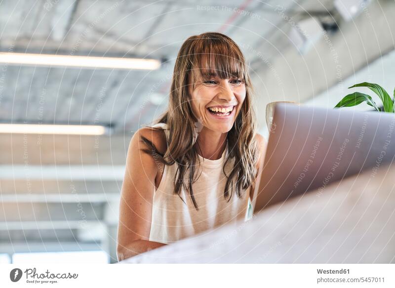 Frau lächelt, während sie zu Hause einen Laptop benutzt Farbaufnahme Farbe Farbfoto Farbphoto Innenaufnahme Innenaufnahmen innen drinnen Tag Tageslichtaufnahme