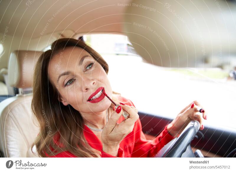 Porträt einer reifen Frau beim Auftragen von Lipgloss im Auto Kleider Rückspiegel KFZ Verkehrsmittel Automobil Autos PKW PKWs Wagen fahrend fahrende fahrender