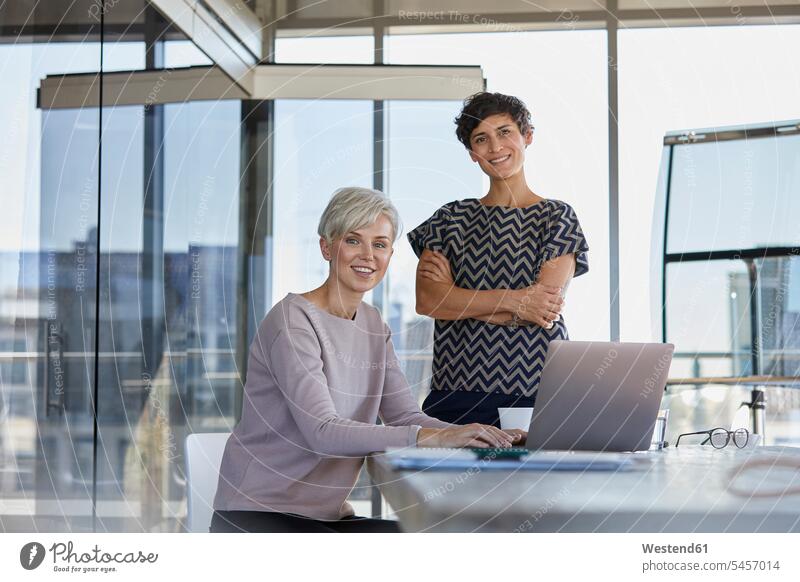Porträt von zwei lächelnden Geschäftsfrauen mit Laptop am Schreibtisch im Büro Arbeitstisch Schreibtische Businesswomen Businessfrauen Businesswoman Office