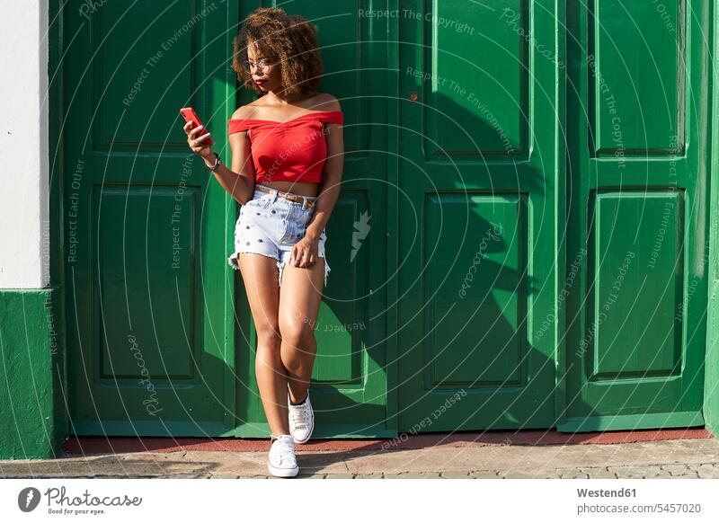 Frau in Rot überprüft ihr Telefon Afrolook Afros Afro-look SMS Textnachricht Top Tops Nachricht Mitteilung Botschaft Drahtlose Technologie drahtlose Verbindung