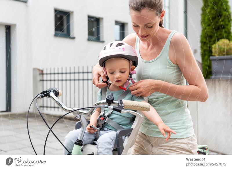 Mutter und Tochter, Tochter mit Helm sitzt im Kindersitz Fahrrad Bikes Fahrräder Räder Rad Mami Mutti Mütter Mama Töchter sitzen sitzend anschnallen