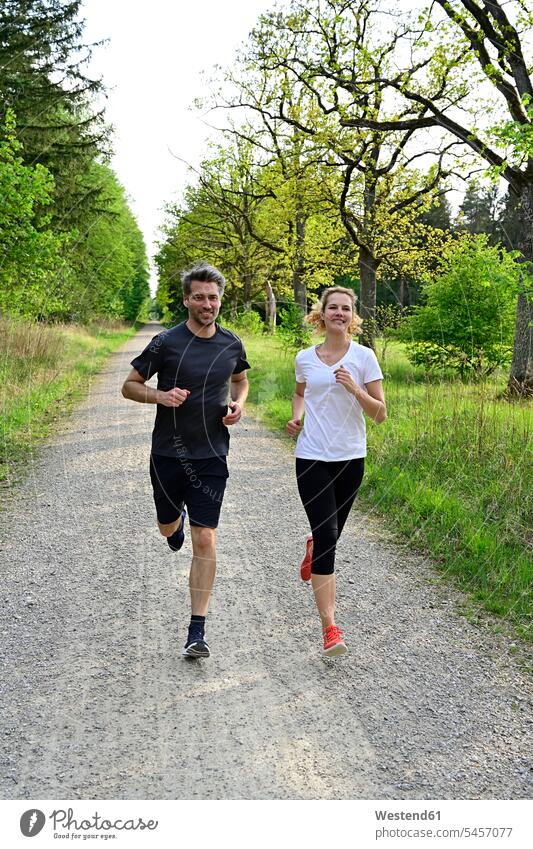 Glückliches Paar joggt auf Feldweg gegen Bäume und Pflanzen im Wald Farbaufnahme Farbe Farbfoto Farbphoto Deutschland Wälder Forst Natur Außenaufnahme außen