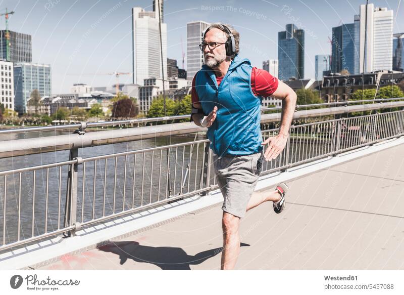 Älterer Mann mit Kopfhörern läuft auf einer Brücke in der Stadt Männer männlich laufen rennen Bruecken Brücken staedtisch städtisch Kopfhoerer Erwachsener