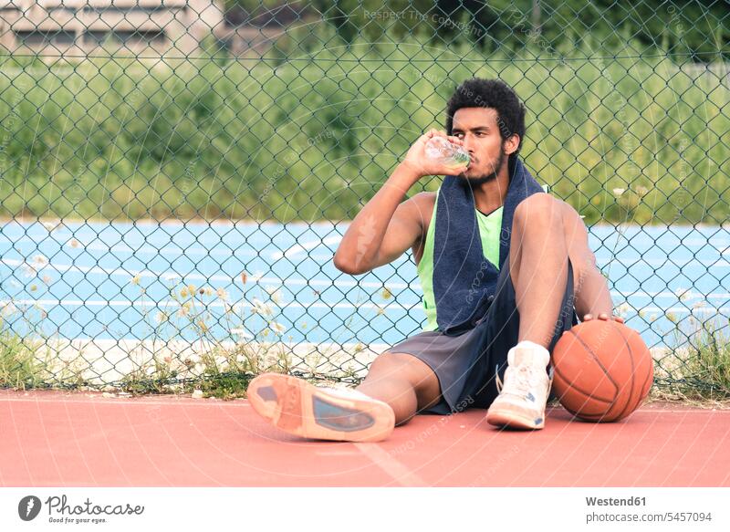 Junger Basketballspieler trinkt aus Wasserflasche Freizeit Muße trinken sitzen sitzend sitzt Flasche Flaschen Wasserflaschen Basketbaelle Basketbälle Pause