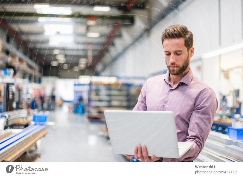 Junger Geschäftsmann benutzt Laptop in Produktionshalle Mann Männer männlich Montagehalle Beruf Berufstätigkeit Berufe Beschäftigung Jobs Business