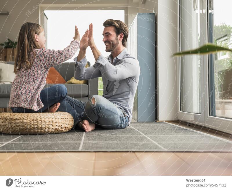 Junger Mann und kleines Mädchen sitzen zu Hause, geben High Five optimistisch Optimismus abklatschen auf dem Boden sitzen auf dem Boden sitzend