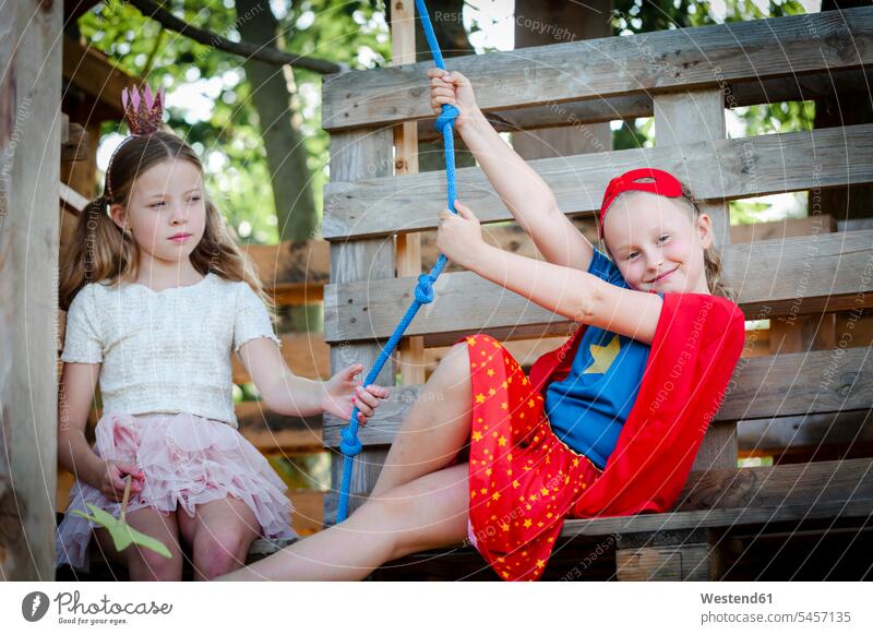 Als Prinzessin und Superwoman verkleidete Mädchen spielen in einem Baumhaus Leute Menschen People Person Personen Held Roecke Röcke Kronen Seile entdecken