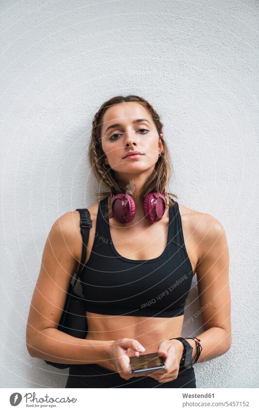 Fitte junge Frau mit einer Smartwatch, die ein Smartphone benutzt stehen stehend steht benutzen benützen Kopfhörer Kopfhoerer trainieren fit üben ausüben Übung