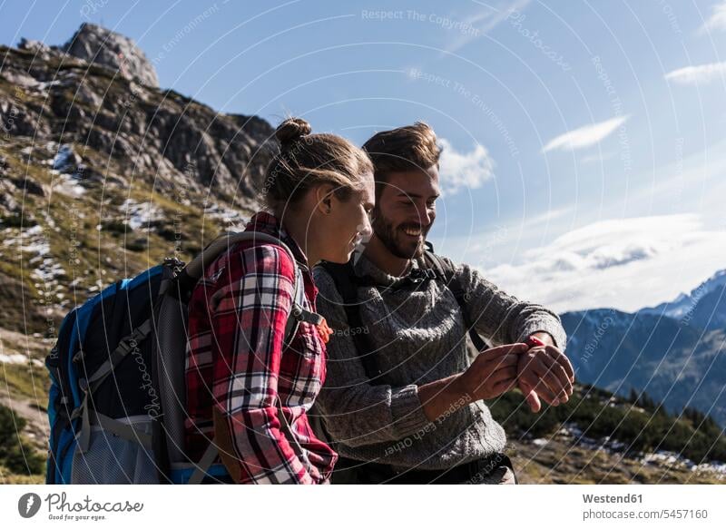 Österreich, Tirol, lächelndes junges Paar schaut auf die Uhr in der Berglandschaft wandern Wanderung Pärchen Paare Partnerschaft Berge ansehen Armbanduhr