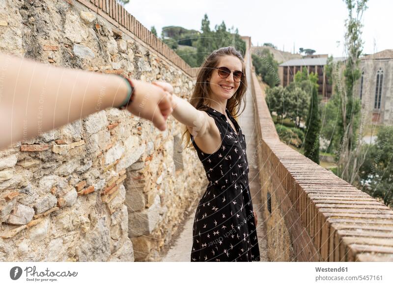 Spanien, Girona, lächelnde Frau hält Männerhand und geht an einer Steinmauer entlang Steinmauern weiblich Frauen Stadt gehen gehend Hand Hände Mauer Mauern Wand
