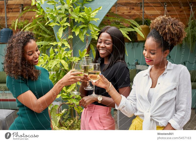 Drei glückliche Freunde stoßen mit Weißwein an Freizeitkleidung casual Freizeitbekleidung Freundinnen Gemeinsamkeit zusammen gemeinsam Zusammenhalt