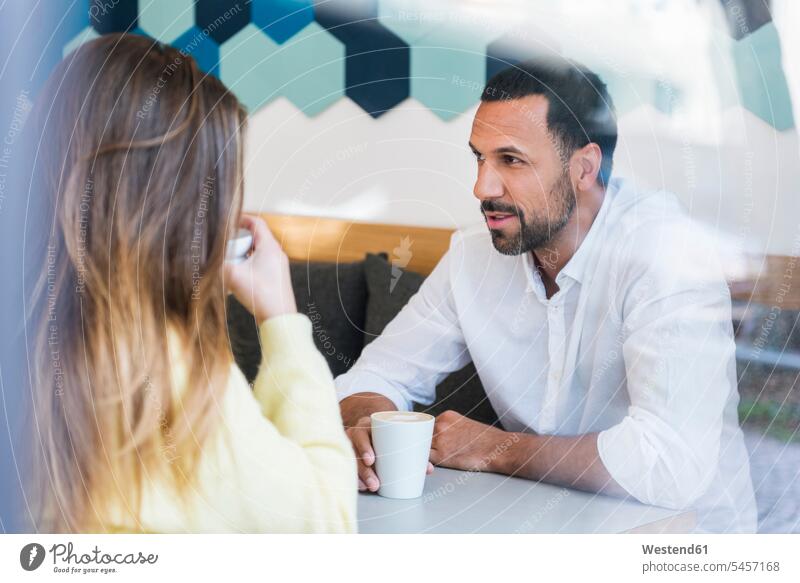 Mann und Frau sitzen in einem Cafe und unterhalten sich Männer männlich Kaffeehaus Bistro Cafes Café Cafés Kaffeehäuser sprechen reden sitzend sitzt Paar