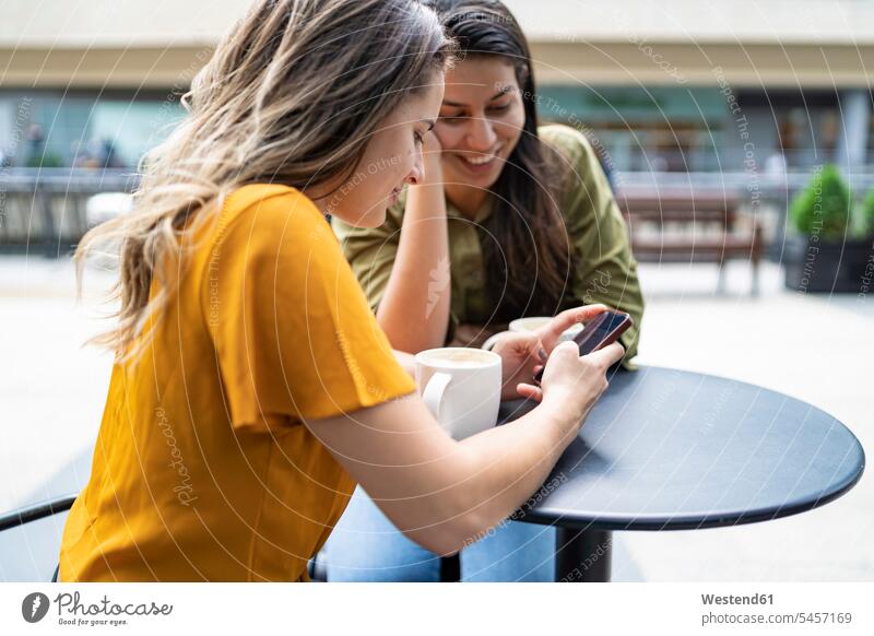 Lesbisches Paar mit Smartphone in einem Straßencafé in der Stadt, London, Großbritannien Telekommunikation telefonieren Handies Handys Mobiltelefon