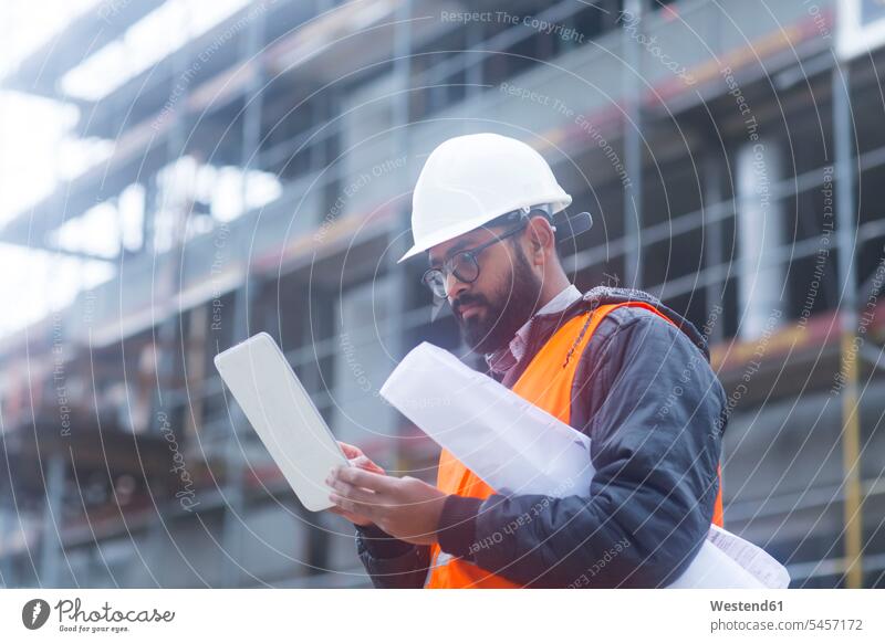 Bauingenieur mit Schutzhelm und Sicherheitsweste mit Tablette auf der Baustelle Job Berufe Berufstätigkeit Beschäftigung Jobs Architekten Ingenieure Karten