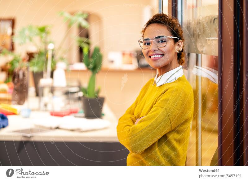 Junge Frau steht in der Tür eines Modegeschäfts, lächelnd stehen stehend junge Frau junge Frauen Boutique Modeladen Brille Brillen Verkäuferin Verkaeuferinnen