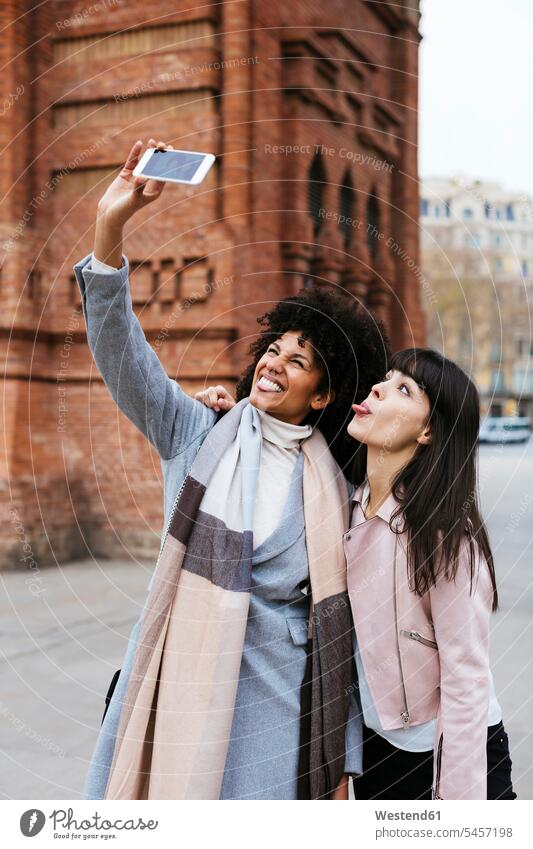 Spanien, Barcelona, zwei verspielte Frauen machen ein Selfie an einem Tor Selfies Tore weiblich glücklich Glück glücklich sein glücklichsein Freundinnen