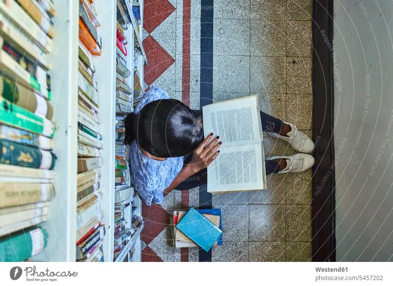 Draufsicht auf eine junge Frau, die auf dem Boden sitzt und in der Nationalbibliothek in Maputo, Mosambik, ein Buch liest Bücher Ablage Regale Bücherregale