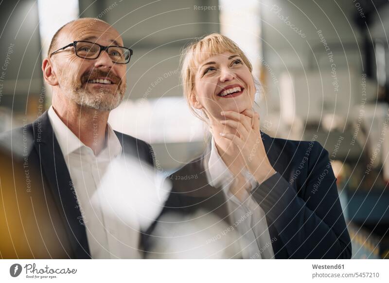 Porträt eines glücklichen Geschäftsmannes und einer glücklichen Geschäftsfrau in einer Fabrik mit Blick nach oben Leute Menschen People Person Personen