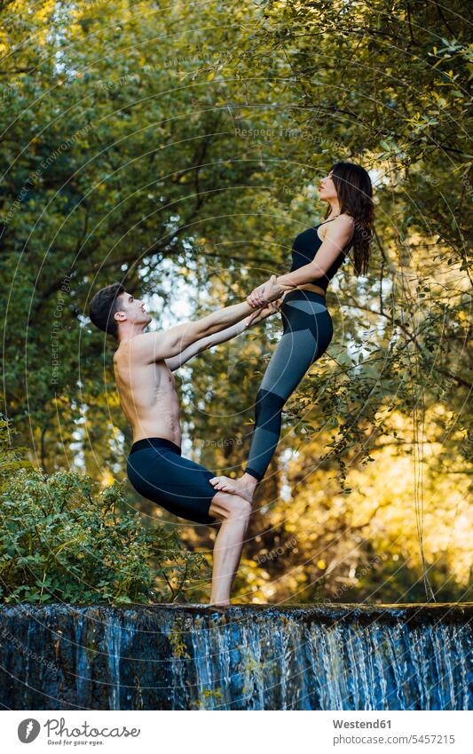 Ein Paar, das gemeinsam Akro-Yoga an einem Wasserfall praktiziert entspannen relaxen ausüben trainieren Übung geniessen Genuss zufrieden stehend steht Muße
