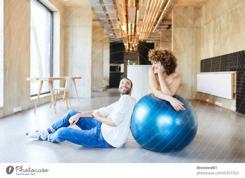 Lächelnder Mann und Frau mit Fitness-Ball im modernen Büro Deutschland Businessmann Achtsamkeit bewusst Bewusstheit achtsam Fitnessball Gymnastikball Sitzball
