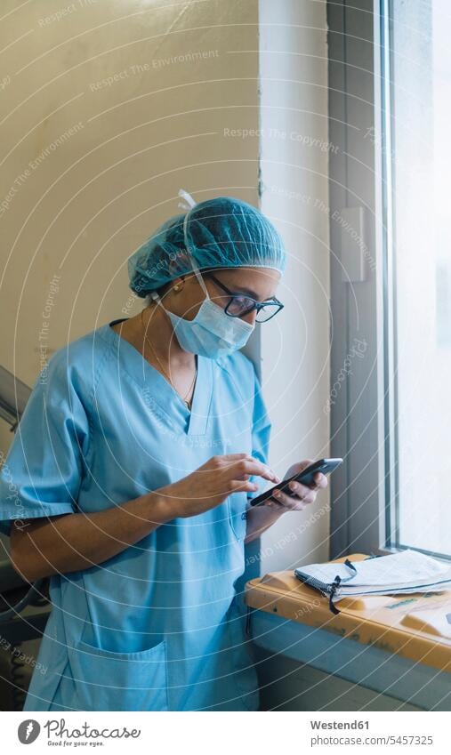 Weiblicher Arzt mit Smartphone im Krankenhaus, Vorbereitung für die Operation Beruf Berufstätigkeit Berufe Beschäftigung Jobs sterile Kleidung vorbereiten