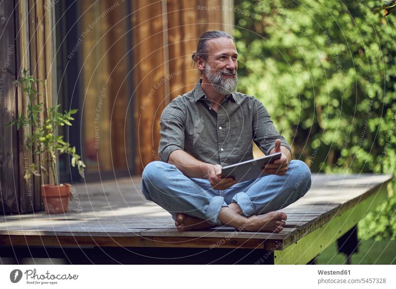 Bärtiger Mann mit digitalem Tablet, der vor einem winzigen Haus sitzt und nachdenkt Farbaufnahme Farbe Farbfoto Farbphoto Deutschland Freizeitbeschäftigung Muße