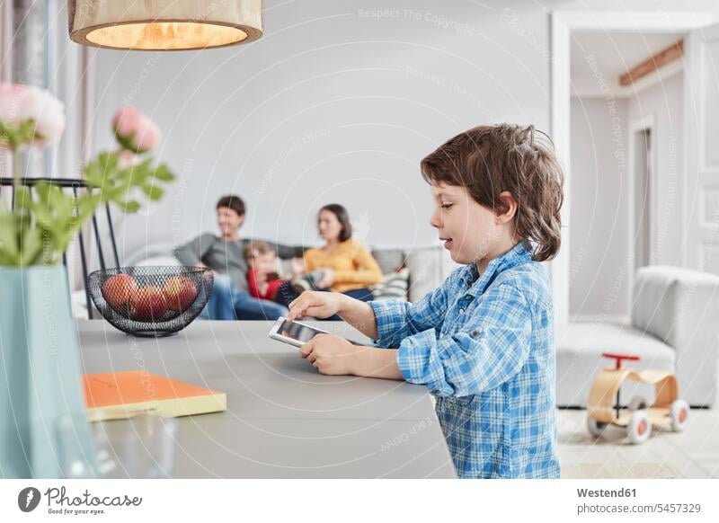Junge betrachtet Tablette zu Hause mit Familie im Hintergrund Zuhause daheim Tablet Computer Tablet-PC Tablet PC iPad Tablet-Computer Buben Knabe Jungen Knaben