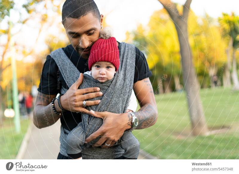 Junger Vater trägt einen kleinen Sohn in einem Tragetuch Leute Menschen People Person Personen gemischtrassig Afrikanisch Afrikanische Abstammung dunkelhäutig
