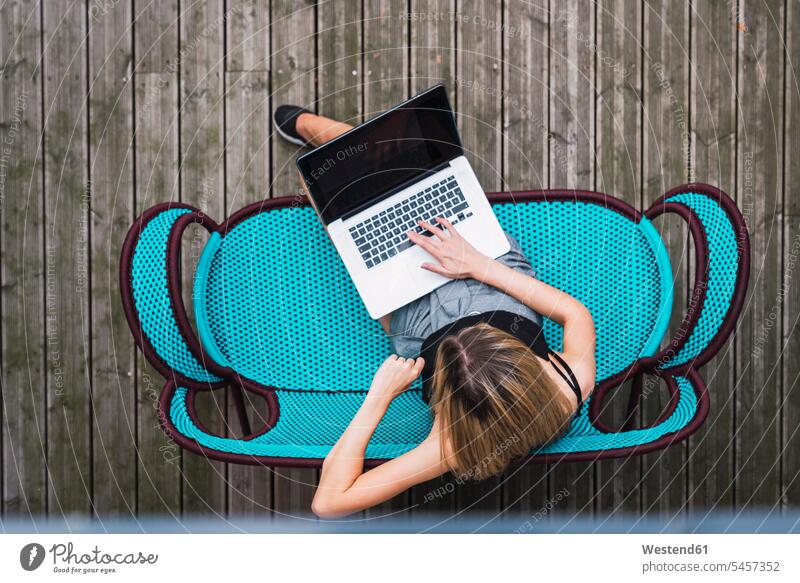 Junge Frau sitzt auf türkisfarbener Couch auf der Terrasse und benutzt einen Laptop, Ansicht von oben Notebook Laptops Notebooks benutzen Terrassen weiblich