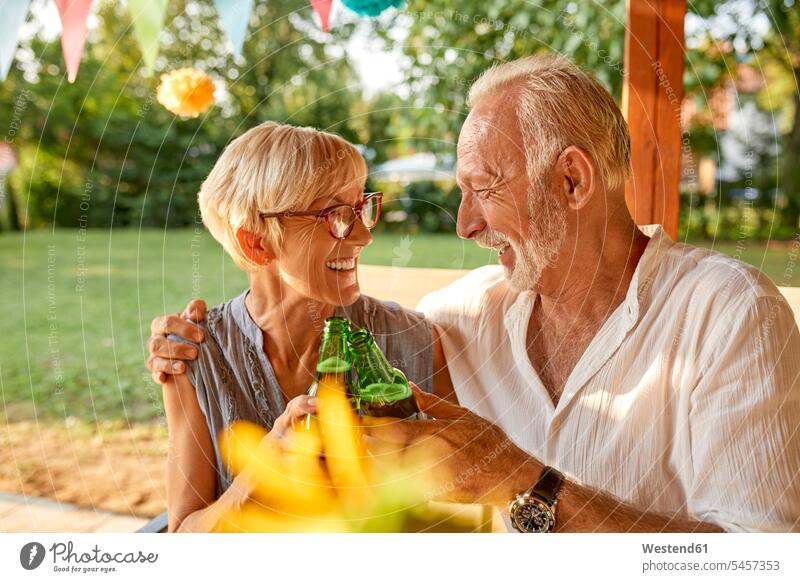 Glückliches älteres Paar stößt auf einer Gartenparty mit Bierflaschen an anstoßen zuprosten anstossen Gartenpartys Gartenfest Gartenfeste Gärten Gaerten Feier