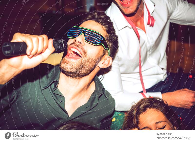 Nahaufnahme eines jungen Mannes, der Karaoke singt, während er mit Freunden in einer Party genießt Farbaufnahme Farbe Farbfoto Farbphoto Innenaufnahme