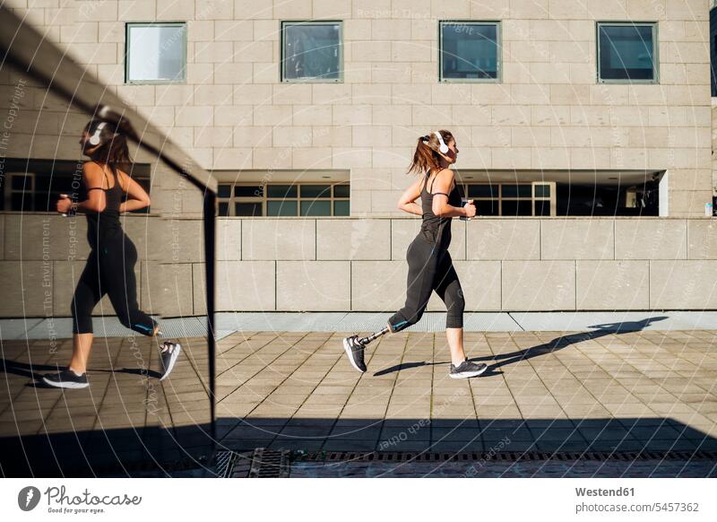 Sportliche junge Frau mit Beinprothese läuft in der Stadt Kopfhoerer hoeren rennen Farben Farbtoene Farbton Farbtöne schwarze schwarzen schwarzer schwarzes fit