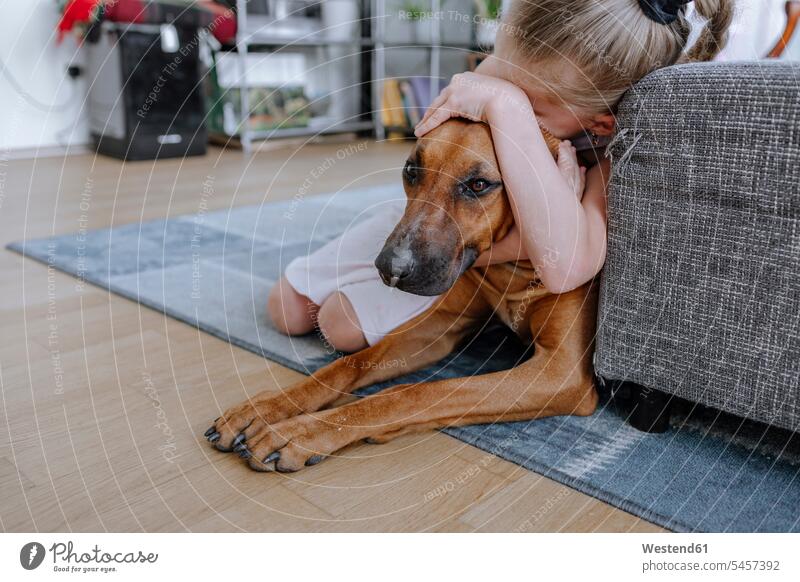 Mädchen umarmt Hund beim Entspannen auf Teppich im Wohnzimmer zu Hause Farbaufnahme Farbe Farbfoto Farbphoto Deutschland Innenausstattung Wohnraum