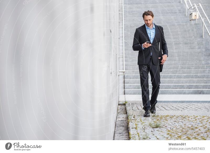 Geschäftsmann zu Fuß auf der Treppe Blick auf Smartphone iPhone Smartphones Treppenaufgang Businessmann Businessmänner Geschäftsmänner Handy Mobiltelefon