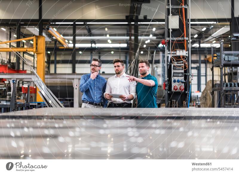 Drei Männer teilen sich Tabletten in der Fabrikhalle Kollegen Arbeitskollegen Produktionshalle Montagehalle Mann männlich Tablet Computer Tablet-PC Tablet PC