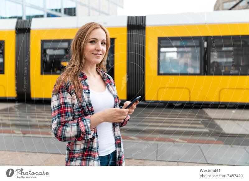 Porträt einer lächelnden Frau in der Stadt mit einer Straßenbahn im Hintergrund, Berlin, Deutschland Transport Transportwesen Bahnen S-Bahn S-Bahnen