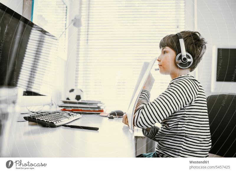 Junge zeigt seine Schulergebnisse zu Hause vor einer Webcam am Computer, Videokonferenz Schüler Kopfhörer hören lernen sitzen zeigen Zuhause Online Verbindung
